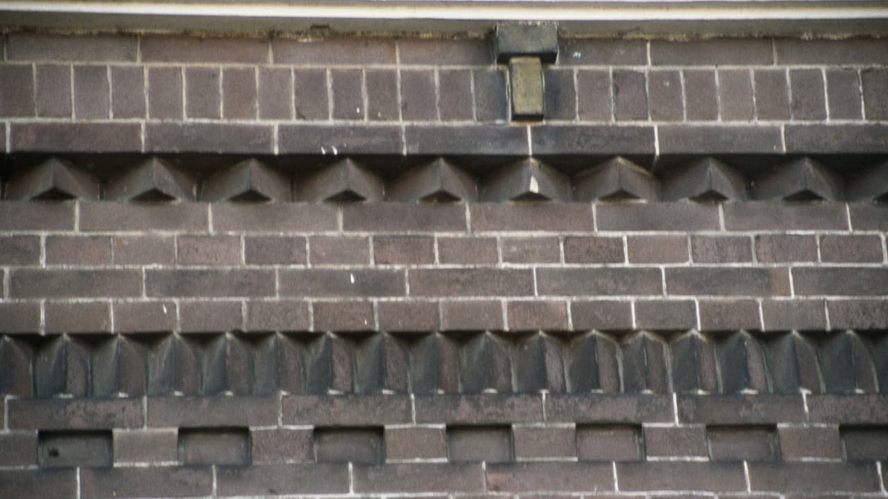 Detail van metselwerk in baksteen, met een band van uitstekende stenen die een patroon vormt.